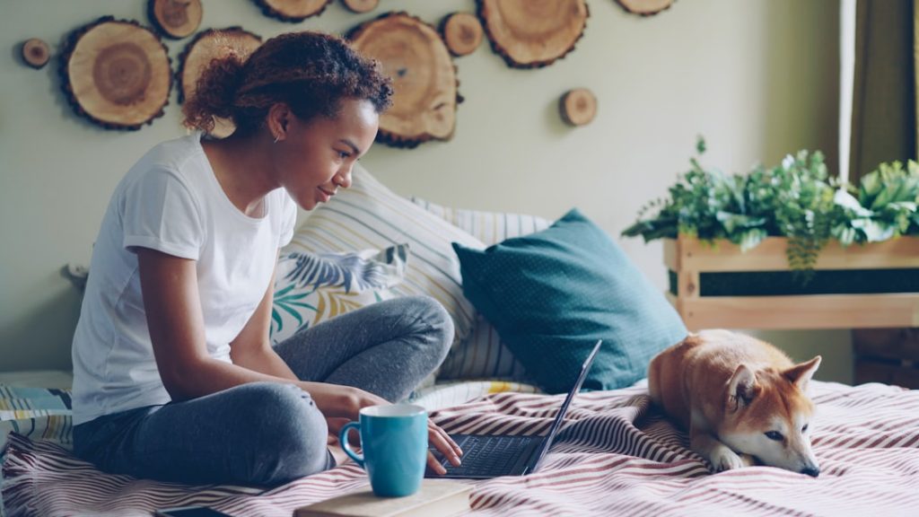 Woman working on a laptop with her dog nearby at home